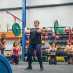 Proud woman weightlifting while her gym mates cheering her on