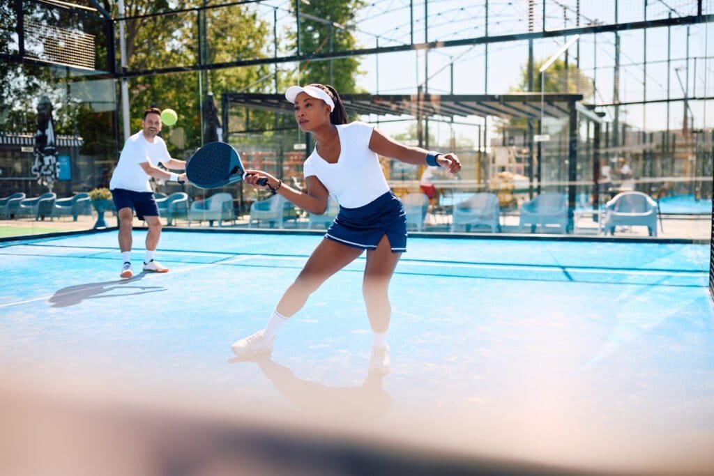 Black athletic woman playing padel in mixed doubles on outdoor court.