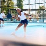 Black athletic woman playing padel in mixed doubles on outdoor court.